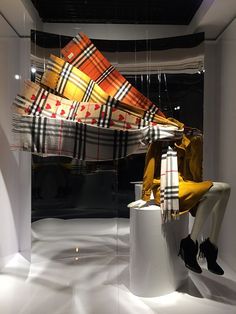 a woman sitting on a stool in front of a window with a scarf hanging from it