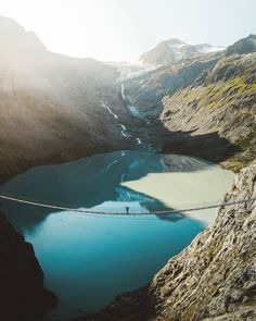 a person walking across a suspension bridge over a mountain lake in the middle of nowhere