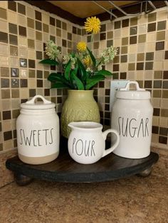 three jars with flowers in them sitting on a counter top next to a vase filled with flowers