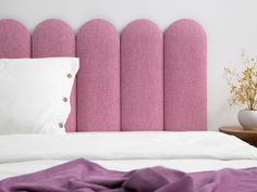 a bed with pink headboard next to a vase on the nightstand and purple blanket