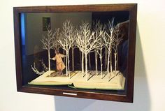 an open book with trees cut out of it in a glass case on the wall