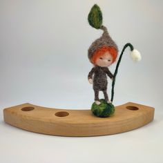 a needled doll is standing on a piece of wood and holding a green plant