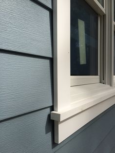 a window on the side of a house with blue siding and white trimmings