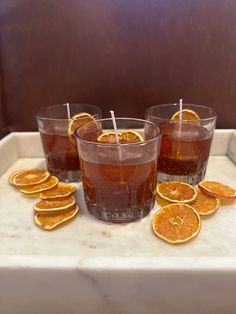 three glasses filled with liquid sitting on top of a white tray covered in orange slices