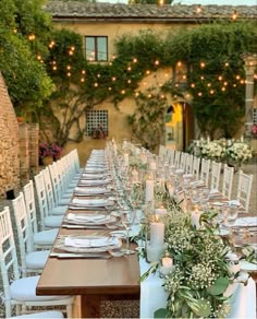 a long table is set with white chairs and place settings for an outdoor dinner party