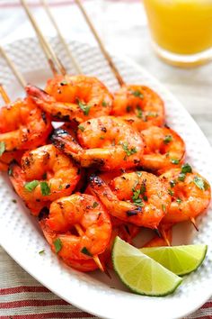 shrimp skewers on a plate with lime wedges and a glass of orange juice