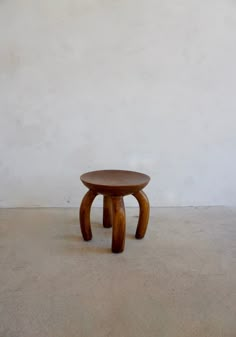 a wooden stool sitting on top of a cement floor next to a white stucco wall