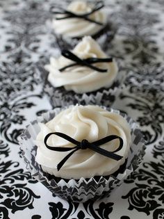 three cupcakes with white frosting and black bows on them sitting on a table