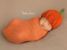 a newborn baby wearing an orange knitted hat with a green leaf on it's side