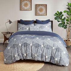 a bed with blue and white comforters in a bedroom next to a plant on the floor