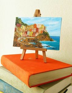 an easel sitting on top of a stack of books next to a painting board