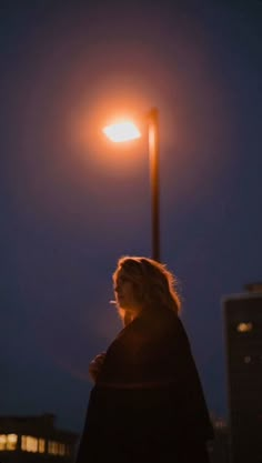 a woman standing under a street light at night with her back turned to the camera