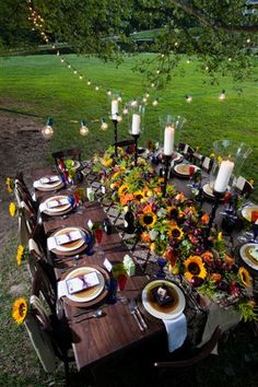 an outdoor dinner table set with sunflowers and candles