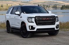 a white truck parked next to a body of water and hills in the background with trees