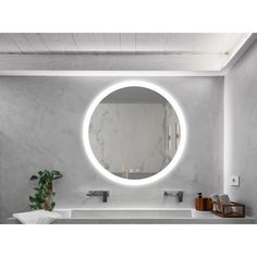 a bathroom sink with a round mirror above it and a potted plant in the corner