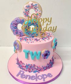 a pink birthday cake with donuts and sprinkles