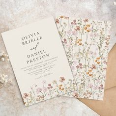 two wedding cards with flowers on them next to some envelopes and paper, one is brown