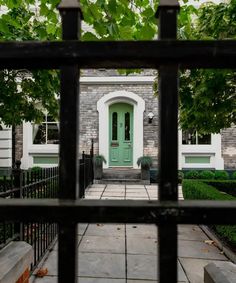 a green door in front of a house through a gated area with trees and bushes