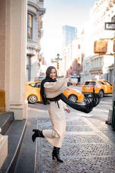 a woman is walking down the street with her scarf around her neck and black boots