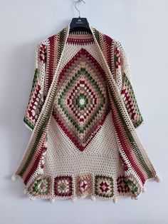 a crocheted sweater hanging on a hanger in front of a white wall