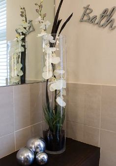 two vases with flowers and balls on a table in front of a bathroom mirror