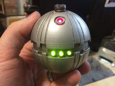 a hand holding a silver toy with green lights on it's face and eyes