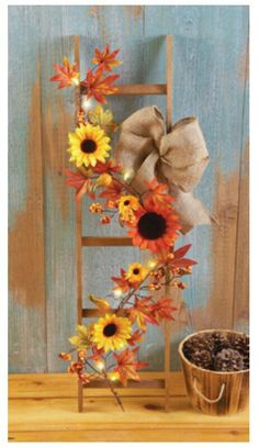 a wooden ladder with sunflowers and a bow on it next to a potted plant