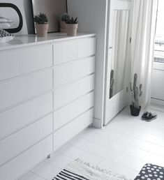 a white dresser sitting in a bedroom next to a window with potted plants on top of it