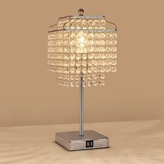 a crystal table lamp with a square base on a beige background, it is lit by a single light bulb