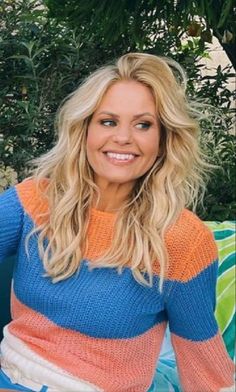 a woman sitting on top of a blue couch next to a green bush and smiling