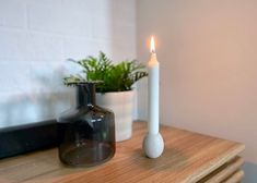 a white candle sitting on top of a wooden table next to a potted plant