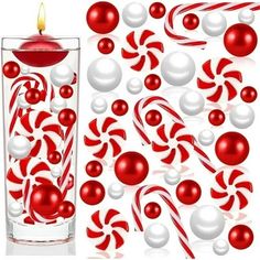 a candle and some candy canes in a glass with red and white balls around it