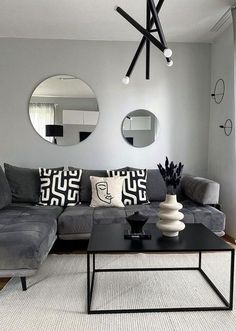 a living room with grey couches and mirrors on the wall above them, along with black tables