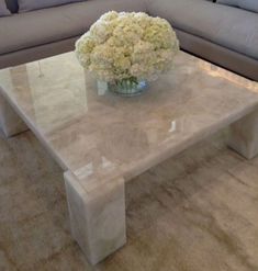 a white marble coffee table with flowers in a glass vase on the top and couches behind it