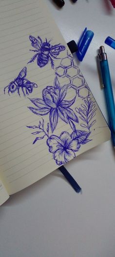 a notebook with flowers and bees on it next to some blue markers, pencils and pens