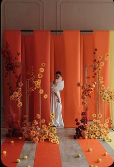 a woman standing in front of an orange and white backdrop with flowers on the floor