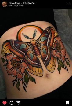 a butterfly tattoo on the side of a woman's stomach with flowers around it