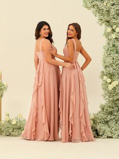 two women standing next to each other in front of a floral arch wearing pink dresses