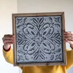 a woman is holding up an ornate tile in front of her face and she has one hand on the frame