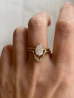 a woman's hand wearing a gold ring with a pear shaped diamond