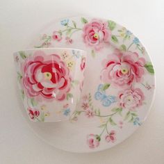 a white plate topped with a pink flowered cup and saucer next to a fork