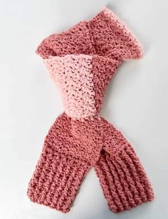 a crocheted pink scarf is laying on top of a white surface and it's folded up