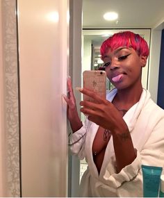 a woman with pink hair brushing her teeth in front of a mirror and taking a selfie