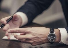 a person sitting at a table writing on a piece of paper with a pen in their hand