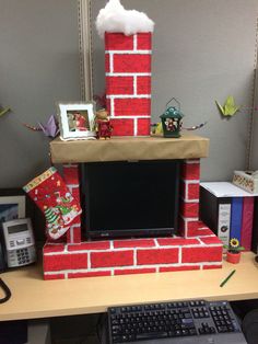 an office cubicle decorated for christmas with a brick fireplace and flat screen tv on the desk