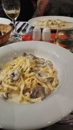 a white plate topped with pasta covered in sauce and mushrooms next to two glasses of wine