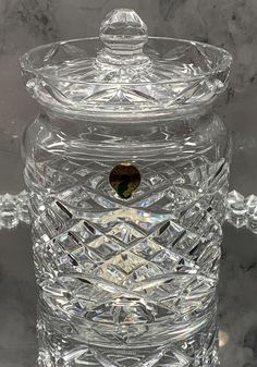 a clear glass jar with a lid and handle sitting on a marble counter top next to a wall