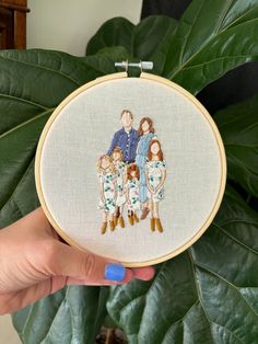 a hand holding a cross stitched family portrait