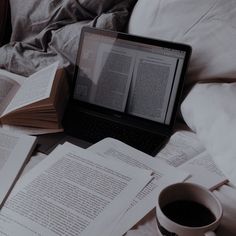 an open laptop computer sitting on top of a bed next to books and a cup of coffee