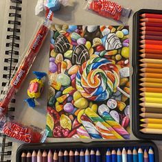 an assortment of colored pencils next to a drawing book with candy art on it